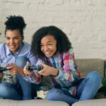 Two smiling girls playing video games on couch.