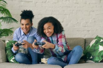 Two smiling girls playing video games on couch.