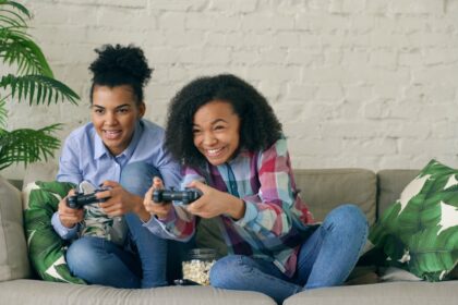 Two smiling girls playing video games on couch.