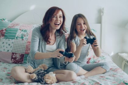 Mother and daughter play video games on a bed.