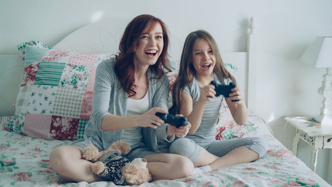Mother and daughter play video games on a bed.