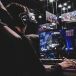 Mikrofon Shure MV7 auf einem schwarzen Stativ vor einem Gaming-Setup mit beleuchteter Tastatur.